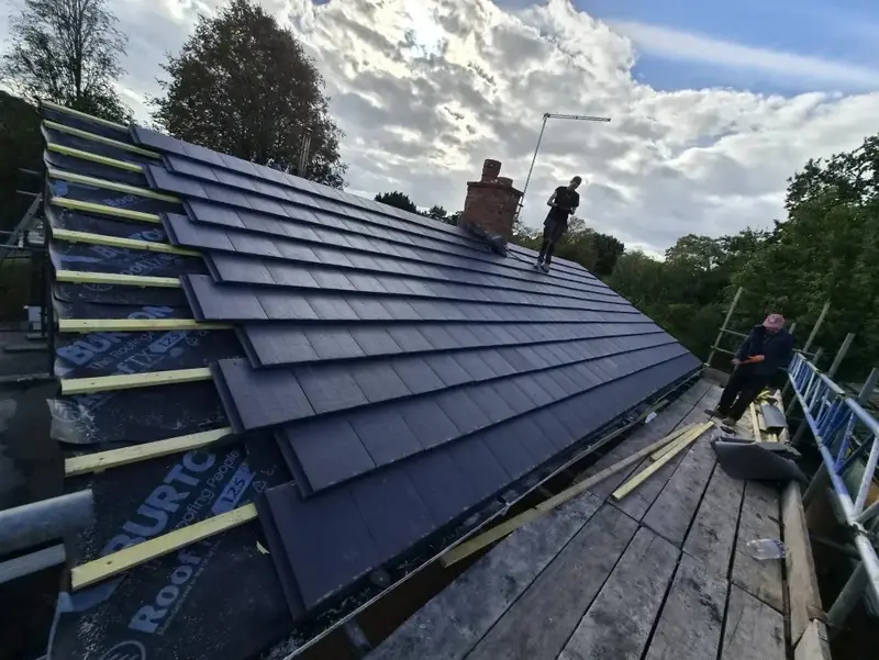 Two roofers laying dark tiles from the top of a scaffold in Edgbaston